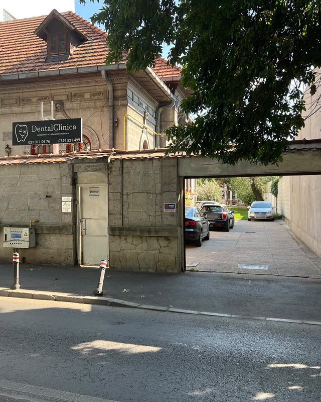DentalClinica văzută din stradă: firma neagră de deasupra zidului de piatră și, în dreapta, poarta de acces în curte